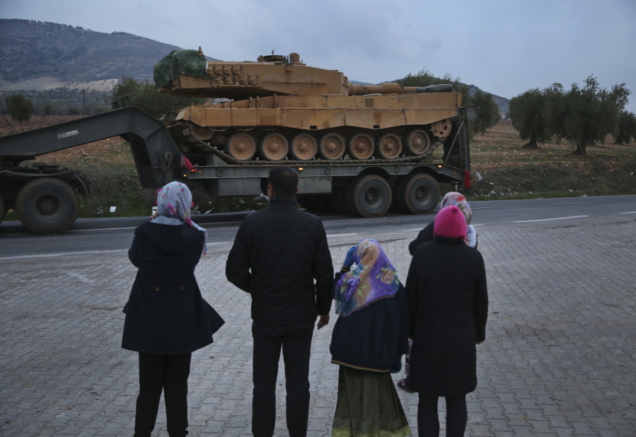 Residents watch as a truck, part of a convoy, transporting a Turkish Army tank is driven in the outskirts of the town of Kilis, Turkey, near the border with Syria, on Sunday. Turkish troops and Syrian opposition forces attacked a Kurdish enclave in northern Syria on Sunday in their bid to drive from the region a U.S.-allied Kurdish militia, which responded with a hail of rockets on Turkish towns that killed at least one refugee.