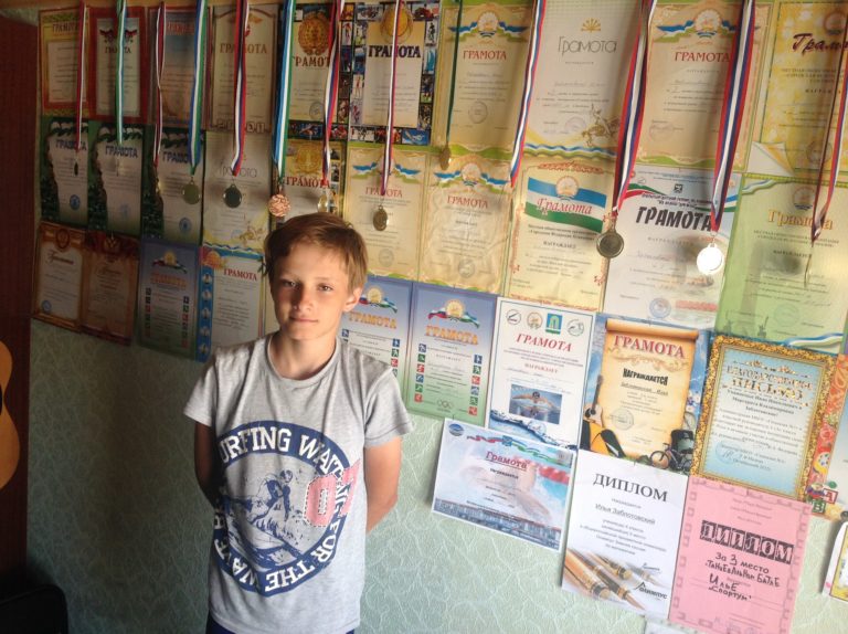 An 11-year old Ilia Zablotoviskii poses in front of a wall of swimming accolades in his native Russia in 2011. Zabolotoviskii now leads Evergreen High School's swim program.
