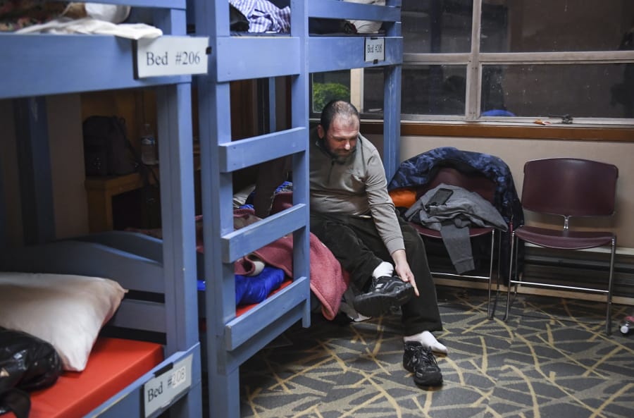 Robert Hardy takes off his shoes at his bed in the Winter Hospitality Overflow shelter at St. Paul Lutheran Church in Vancouver earlier this month. St. Paul Lutheran Church is one of two churches that have long hosted the WHO shelter in Clark County, providing men with a meal and safe place to sleep.