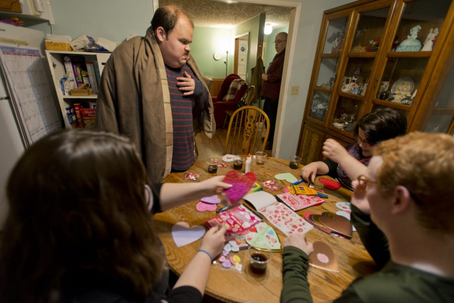 Art night with the Otton family (and some friends). Geoffrey Otton, at center in brown blanket, is 29 and lives with severe autism. Every Saturday night his family, friends and neighbors gather to visit him and each other during a brief social hour — while keeping their hands busy with simple art projects like making valentines. On a recent Saturday he was joined by Mariah Huerena, 17 (left), Hunter Yost, 18, and sister Linda Otton, 26. Geoffrey’s father, Ed Otton, in the background, was nursing a cold and staying away from the company that night.