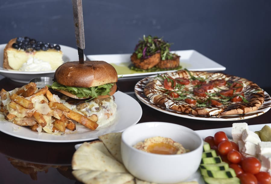 Offerings from Luxe include, clockwise from left, a Gorgonzola burger with Parmesan garlic fries, a slice of blueberry lemon curd cheesecake, crab cakes, a Margherita pizza and the hummus plate.