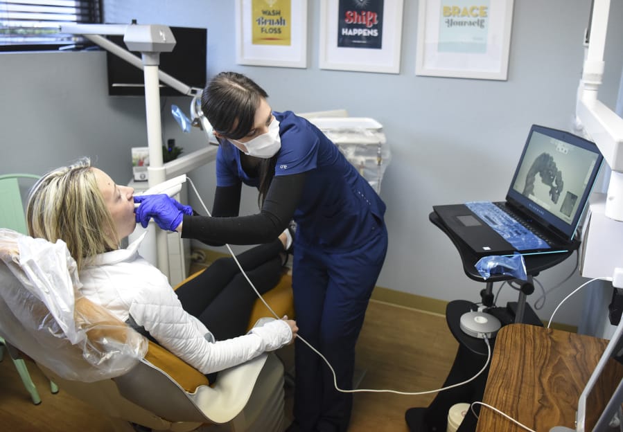 Rachel Haebe, of Vancouver, left, waits patiently while dental assistant Libby Mayea uses an intraoral scanner to digitally map Haebe’s teeth. The map will be used to create invisible aligners to help straighten her teeth and correct her bite. Natalie Olsen, of Vancouver, co-founded the company to make fixing teeth more affordable.
