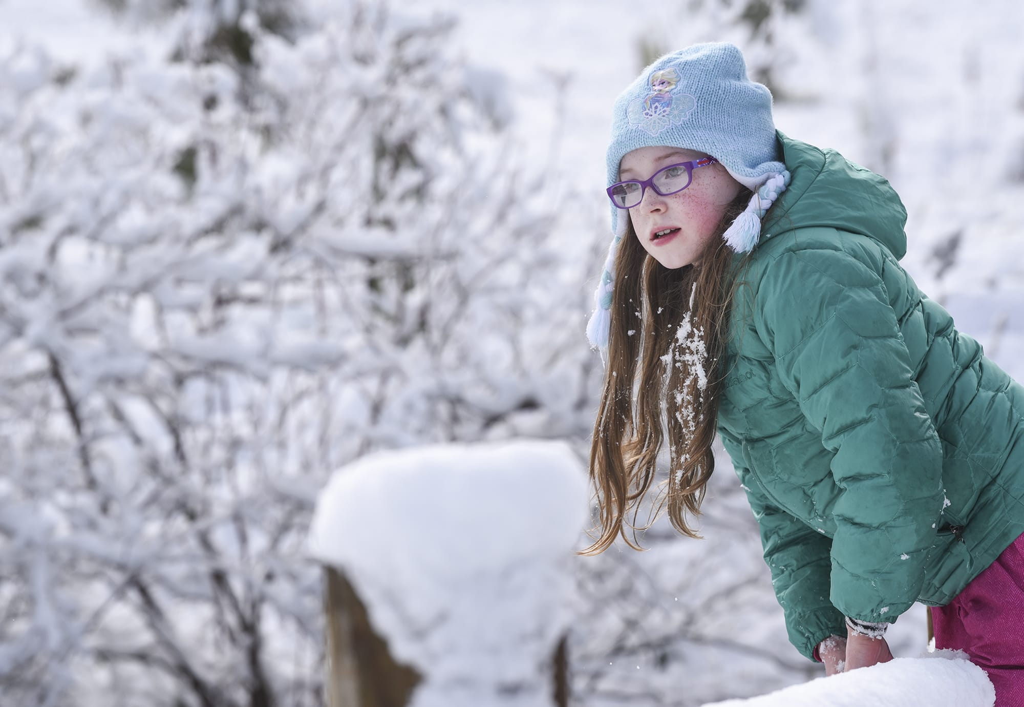 Eden Stahley, 9, leans over a snow-covered fence to look into a marsh at Mount Vista near WSU Vancouver, Monday morning, February 19, 2018. Stahley and her two sisters were enjoying the few inches of snow by sledding together on a hill near their home.