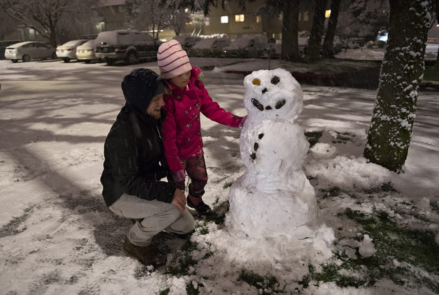 Martin Bizjack of Vancouver and his daughter, Ellen, 7, put the finishing touches on their snowman in Southeast Vancouver while playing in the winter weather Tuesday night.