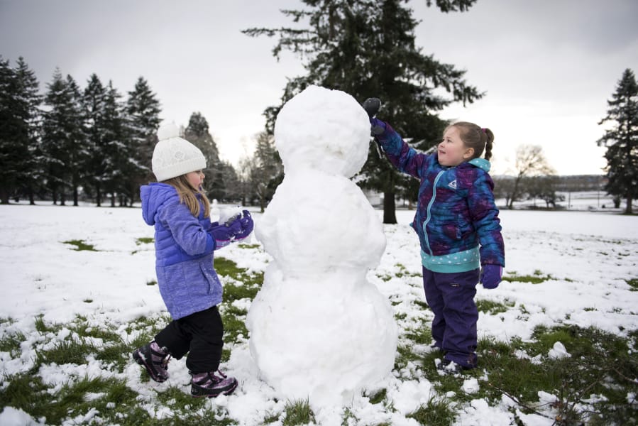 Juliana Pazz, 3, and her friend Remi Helus, 4, both of Vancouver, make a snowman at Fort Vancouver National Site on Thursday morning. Many local schools operated with a late start on Thursday morning.