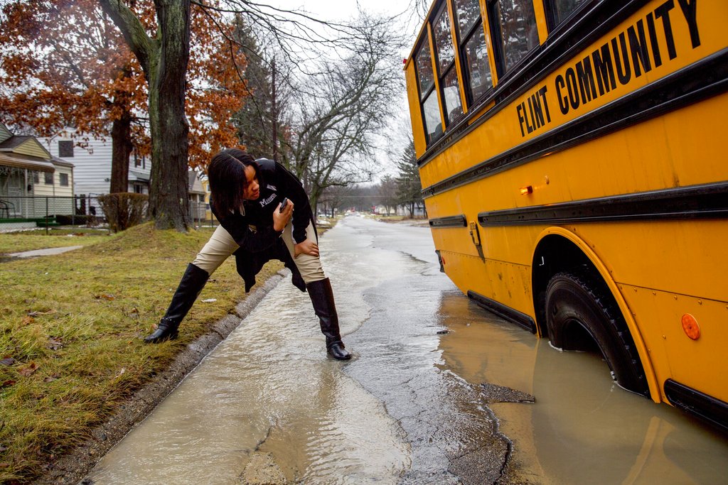 Ketara Sealey, 17, takes a photo of the school bus' tire on Tuesday, Feb. 20, 2018, in Flint, Mich. The bus became stuck when its tire fell into a hole due to high flood waters. High water closed roads in Michigan.