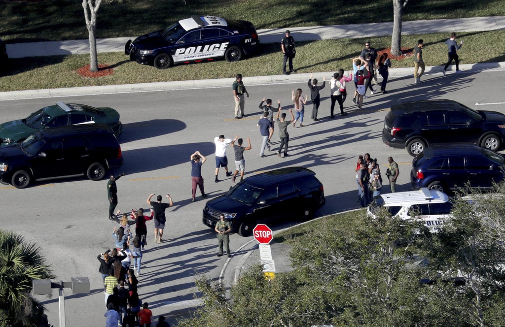 FILE - In this Wednesday, Feb. 14, 2018 file photo, students hold their hands in the air as they are evacuated by police from Marjory Stoneman Douglas High School in Parkland, Fla., after a shooter opened fire on the campus. A week after a shooter slaughtered more than a dozen people in the Florida high school, thousands of protesters, including many angry teenagers, swarmed into the state Capitol on Wednesday, Feb. 21, calling for changes to gun laws, a ban on assault-type weapons and improved care for the mentally ill.