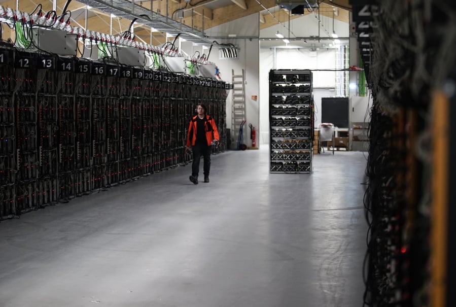 In this photo taken on Jan. 17, 2018, a worker walks along a row of computer rigs that run around the clock ‘mining’ bitcoin inside the Genesis Mining cryptocurrency mine in Keflavik, Iceland. Hand in hand with the rise of bitcoin is a soaring cost of “mining” the cryptocurrency. The energy demand has developed because of the soaring cost of producing the cryptocurrency, which requires computers solving math formulas to mine the 4.2 million coins still available.