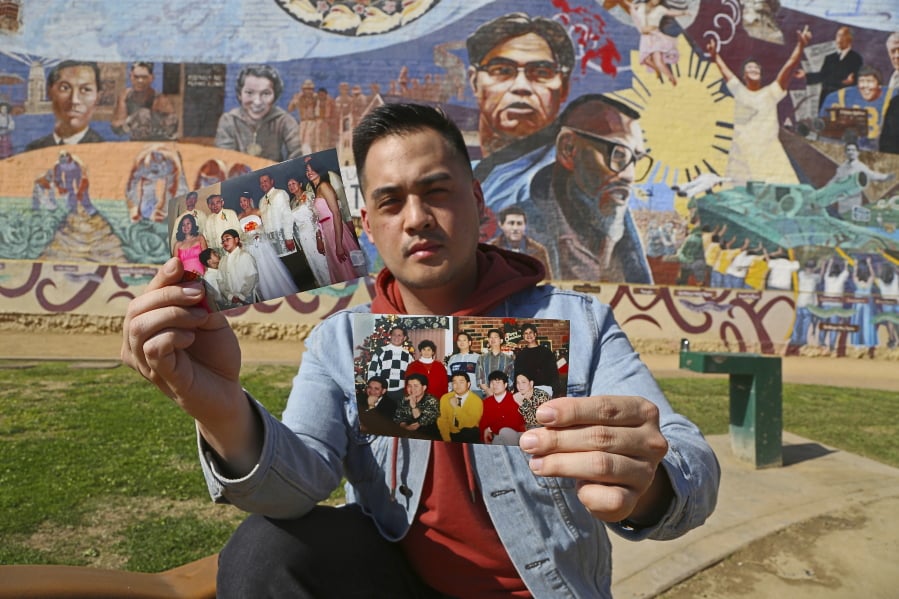 Filipino American Jeff DeGuia, 28, holds up family pictures at Unidad Park in Los Angeles. DeGuia, 28, says it took his mother more than a decade to bring two sisters from the Philippines. “There’s definitely this idea you are not really complete without your huge family,” said DeGuia, whose grandfather came to the United States for an engineering job in the 1970s. In the background is Eliseo Art Silva’s mural “Gintong Kasaysayan, Gintong Pamana,” A Glorious History, A Golden Legacy.