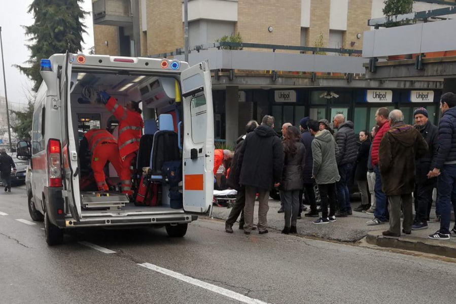 Paramedics, background center, attend a wounded man after a shooting broke out in Macerata, Italy, Saturday, Feb. 3, 2018. Italian police arrested a lone gunman in a series of drive-by shootings targeting foreigners Saturday morning that paralyzed a small central Italian city still reeling from the gruesome murder of a young Italian woman allegedly at the hands of a Nigerian immigrant.