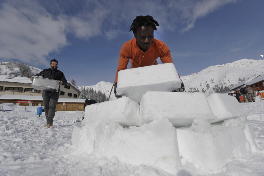 In this photo taken on Friday, Feb. 2, 2018, Omar Kanteh, of Gambia, carries a block of ice as he helps build an igloo with Davide Midali, owner of an igloo village in San Simone di Valleve, near Bergamo, northern Italy. Migrants from African nations far from the frozen north picked up the art of igloo making to help a local restaurant owner realize a project to lure tourists back to this dying mountain resort.