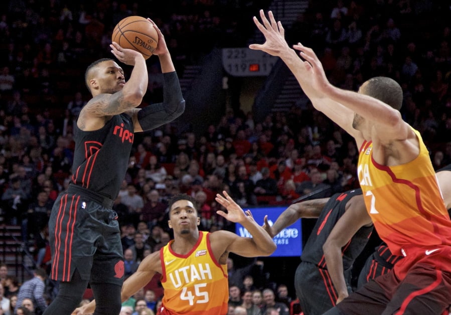 Portland Trail Blazers guard Damian Lillard, left, shoots over Utah Jazz guard Donovan Mitchell, center and center Rudy Gobert, right, during the first half of an NBA basketball game in Portland, Ore., Sunday, Feb. 11, 2018.
