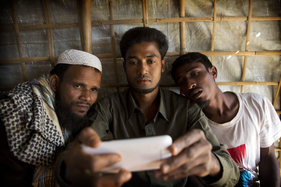 Rohingya Muslim refugee Mohammad Karim, 26, center, shows a mobile video of Gu Dar Pyin’s massacre to other refugees in Kutupalong refugee camp, Bangladesh. On Sept. 9, a villager from Gu Dar Pyin, captured three videos of mass graves that were time-stamped between 10:12 a.m. and 10:14 a.m., when he said soldiers chased him away. When he fled to Bangladesh, Karim removed the memory card from his phone, wrapped it in plastic and tied it to his thigh to hide it from Myanmar police.