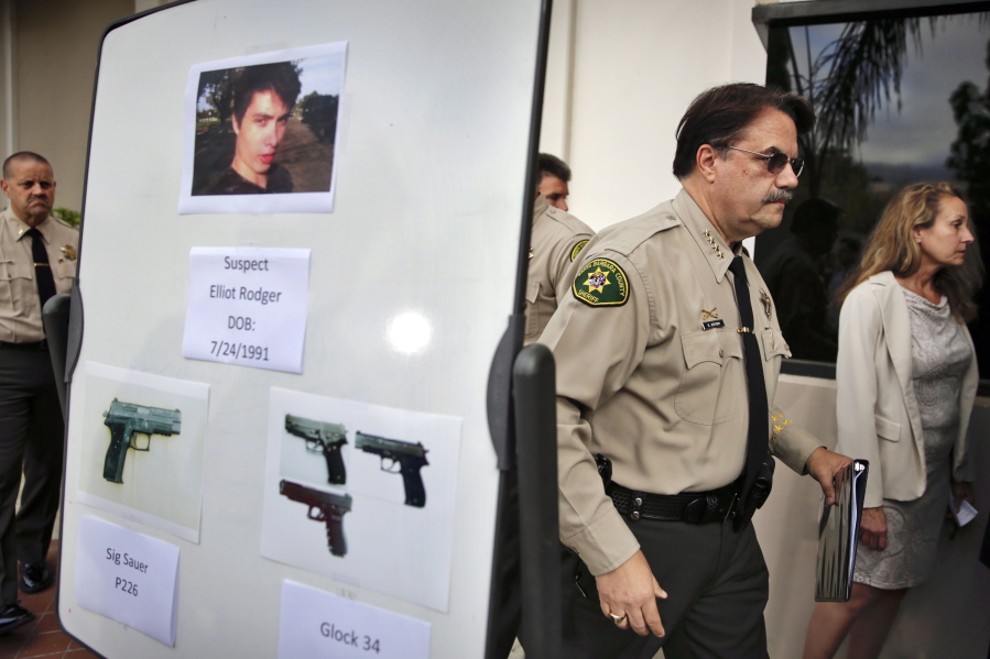 FILE - In this May 24, 2014 file photo, Santa Barbara County Sheriff Bill Brown, right, walks past a board displaying photos of gunman Elliot Rodger and the weapons he used in a mass shooting in Isla Vista, Calif., after a news conference in Santa Barbara, Calif. A growing number of states have passed laws or are considering bills allowing courts to temporarily remove guns from individuals deemed a danger to themselves or others, an intervention that advocates say stops shootings and suicides by disturbed individuals. (AP Photo/Jae C.