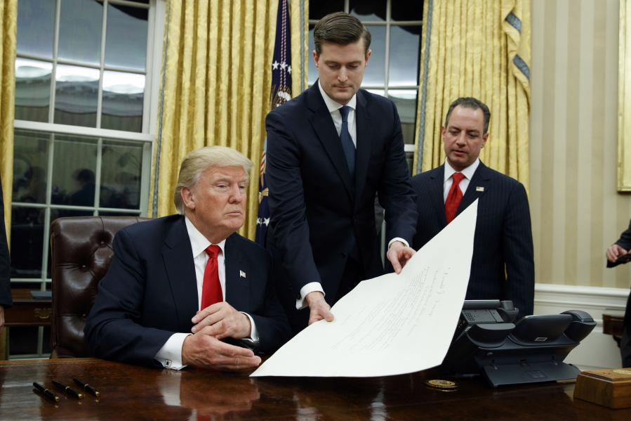FILE - In this Jan. 20, 2017 file photo, White House Staff Secretary Rob Porter, center, hands President Donald Trump a confirmation order for James Mattis as defense secretary, in the Oval Office of the White House in Washington, as White House Chief of Staff Reince Priebus, right, watches. Porter is stepping down following allegations of domestic abuse by his two ex-wives.