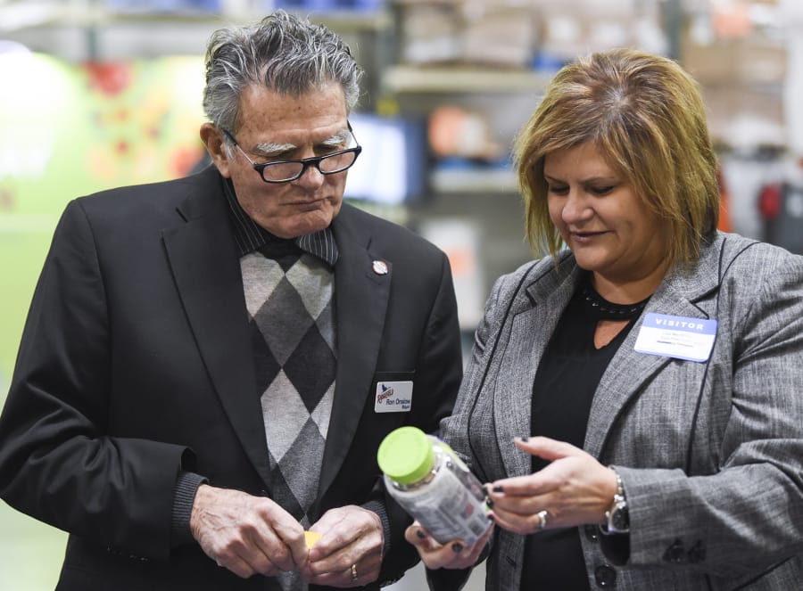 Ridgefield Mayor Ron Onslow looks at a bottle of Vitafusion chewable vitamins with Church & Dwight Co. Inc. Vice President of Sales Lisa MacMillin on Dec. 14, at an event in Vancouver. Onslow is stepping down as mayor after 10 years in office.
