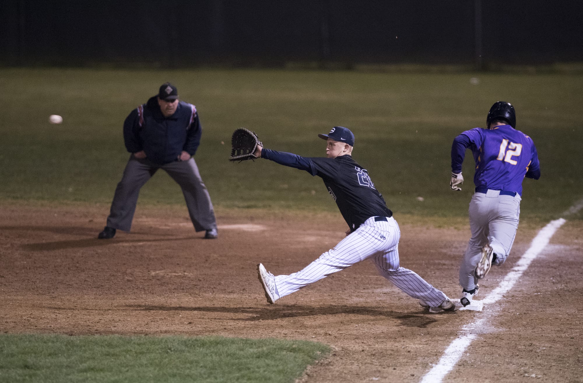 Skyview's Michael Lundgren (20) stretches forward for a catch to gain an out against Columbia River's Nick Nygard (12) as Nygard runs late into first during Friday night's game at Propstra Stadium in Vancouver on March 9, 2018. Columbia River won the season-opener 8-2.