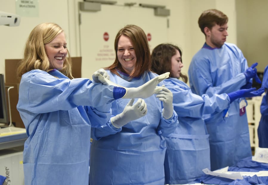 Washington State University medical students Morgan Black, 26, of Spokane, left, and Megan Short, 27, of Vancouver, laugh as Black attempts to properly put on her surgical glove during a workshop on gowning and gloving for the operating room. First-year medical students spent several hours Monday afternoon learning from the staff at Legacy Salmon Creek Medical Center. They’re in town all week.