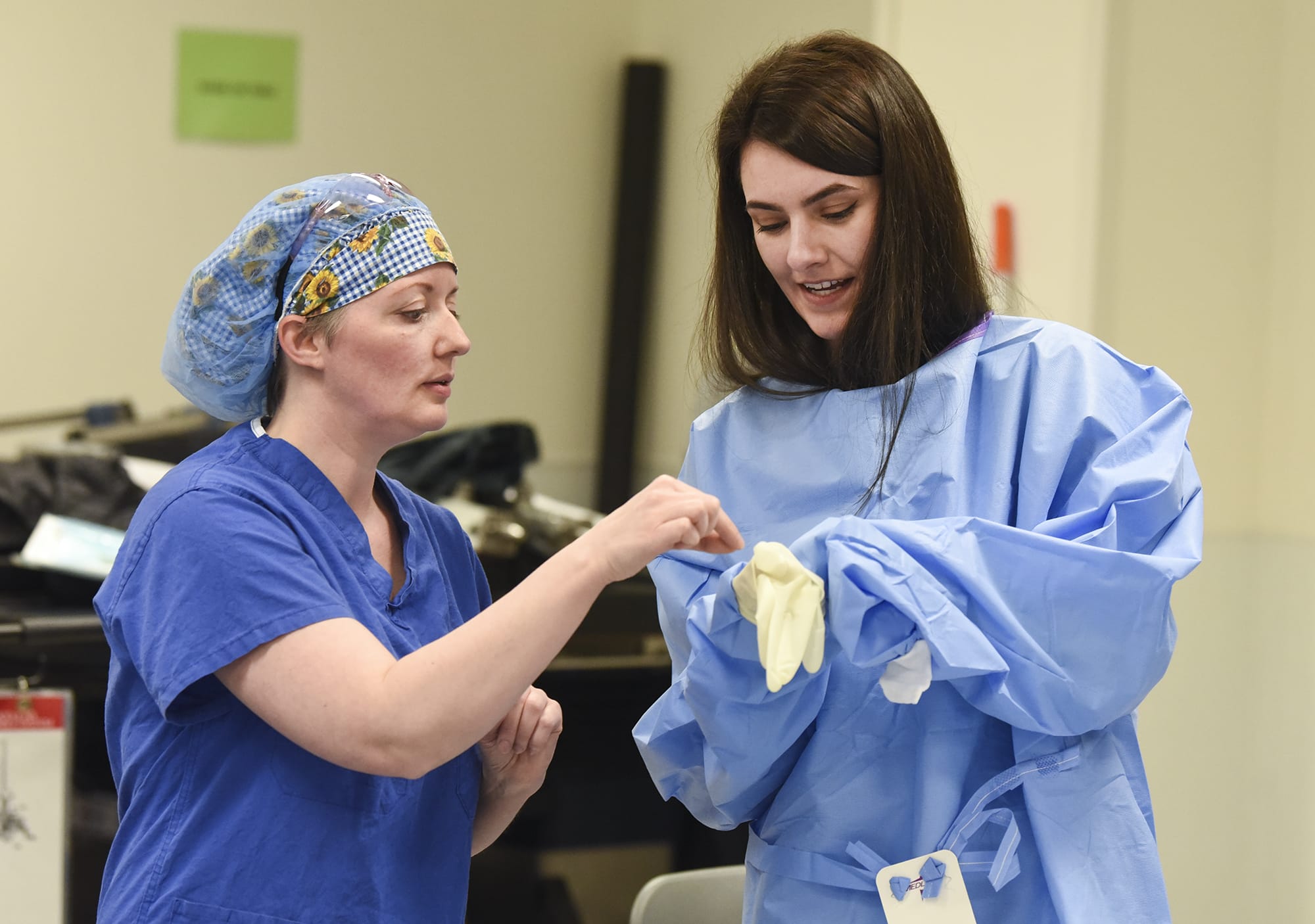 Joanie Yocum, the robotics coordinator for urology and gynecology at Legacy Salmon Creek Medical Center, left, assists Anndres Olson, 26, a student in the Elson S. Floyd College of Medicine at Washington State University, as she attempts to put on a glove following sterile procedures for a lesson on scrubbing for surgeries at Legacy Salmon Creek, Monday March 26, 2018.