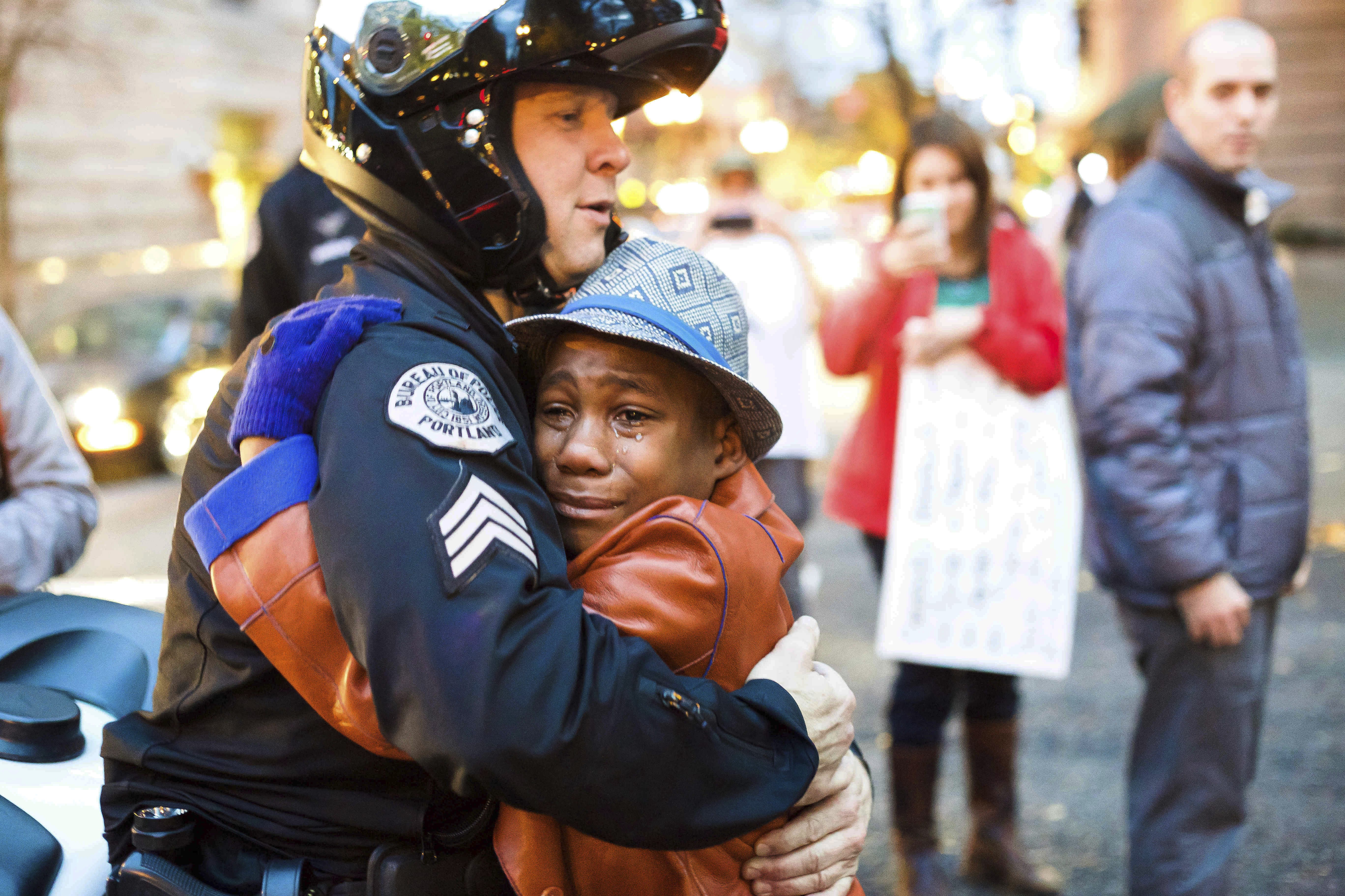 FILE - In this Nov. 25, 2014, file photo provided by Johnny Nguyen, Portland police Sgt. Bret Barnum, left, and Devonte Hart, 12, hug at a rally in Portland, Ore., where people had gathered in support of the protests in Ferguson, Mo. Authorities have said two women and three children were killed Monday, March 26, 2018, when their SUV fell from a cliff along Pacific Coast Highway in Mendocino County. Hart is one of the three other children still missing after the vehicle fell off a cliff. He had gained fame when this picture of him hugging the white police officer during the protest went viral.