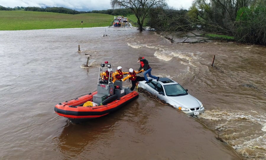This drone photo from video provided by the California Governor’s Office of Emergency Services shows firefighters from the Folsom, Calif., Fire Department rescuing a motorist whose car became stuck as a flash flood washed over a road near Folsom Thursday, March 22, 2018. A powerful storm spread more rain across California on Thursday, swelling rivers, flooding streets and causing some mud and rock slides but, so far, sparing communities a repeat of the disastrous debris flows that hit during a downpour early this year. (Kelly B.