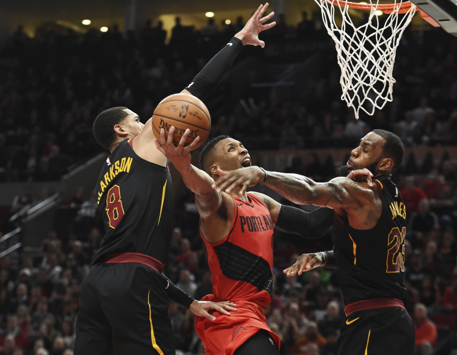 Portland Trail Blazers guard Damian Lillard drives to the basket on Cleveland Cavaliers guard Jordan Clarkson, left and forward LeBron James, right, during the second half of an NBA basketball game in Portland, Ore., Thursday, March 15, 2018. The Blazers won 113-105.