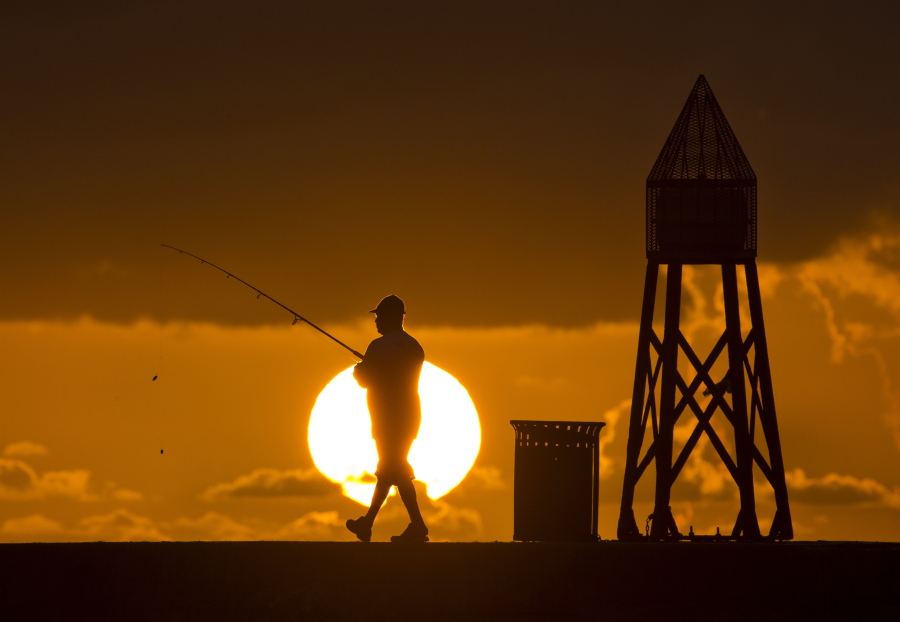 FILE - In this July 14, 2016, file photo, a fisherman prepares to cast a line as the sun rises behind him as he fishes off a jetty into the Atlantic Ocean, in Bal Harbour, Fla. Florida will join most of the nation Sunday, March 11, 2018, in springing ahead, moving clocks up one hour to observe daylight saving time. If Sunshine State legislators get their way, there soon will be no falling back.