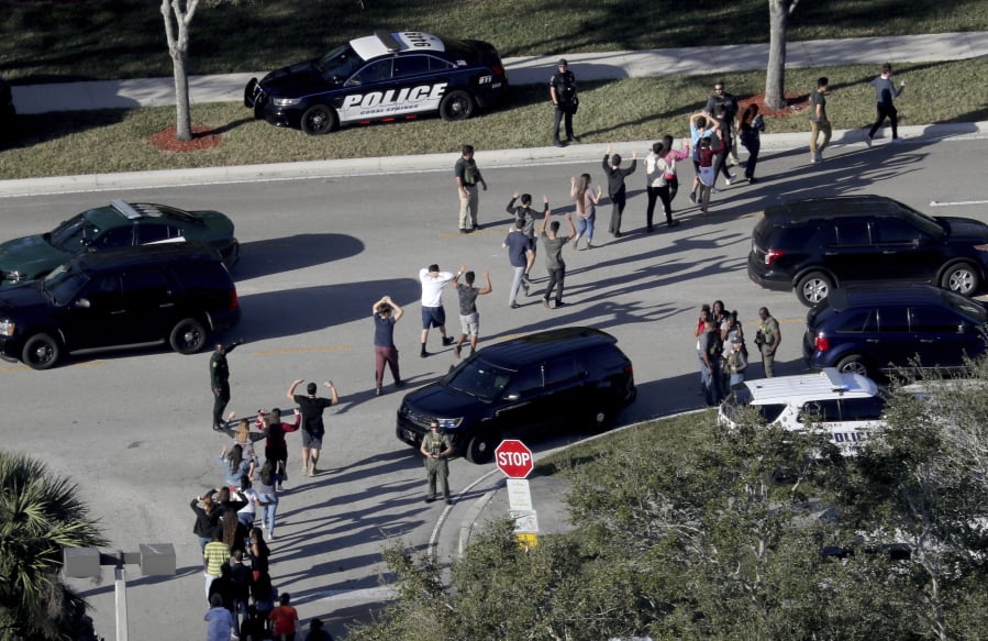 In this Feb. 14, 2018 file photo, students hold their hands in the air as they are evacuated by police from Marjory Stoneman Douglas High School in Parkland, Fla., after a shooter opened fire on the campus. Emergency calls from parents and students during the Florida high school massacre show 911 operators at first trying to grasp the enormity of the emergency and then calmly trying to gather information to assist arriving law enforcement officers. The officers arrive to find chaos as delays allowed the shooter to flee.
