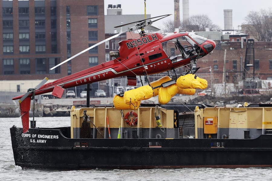 FILE - In this March 12, 2018 file photo, a helicopter is hoisted by crane from the East River onto a barge in New York after a Sunday night crash. The crash is prompting regulators to temporarily ground “doors off” flights using tight restraints that could trap people in an emergency. The Federal Aviation Administration ordered the ban on Friday amid concerns such harnesses prevented passengers from escaping. Five people were killed.