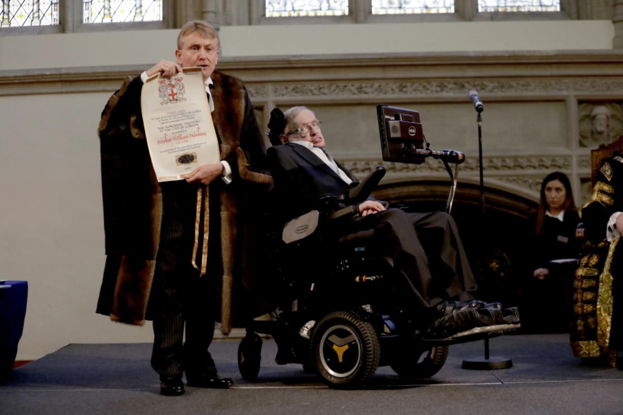 FILE - In this March 6, 2017 file photo, Britain’s Professor Stephen Hawking is presented with his illuminated Freedom scroll by the Chamberlain of the City of London Peter Kane as he receives the Honorary Freedom of the City of London during a ceremony at the Guildhall in the City of London. Hawking, whose brilliant mind ranged across time and space though his body was paralyzed by disease, has died, a family spokesman said early Wednesday, March 14, 2018.
