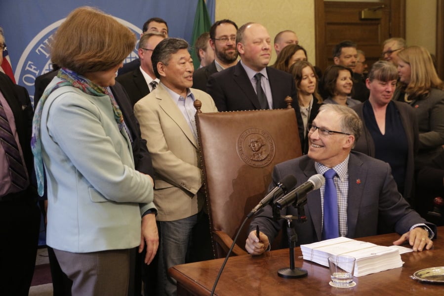 Gov. Jay Inslee, seated, speaks with Democratic Sen. Christine Rolfes, left, before signing the supplemental budget, on Tuesday, March 27, 2018, in Olympia, Wash. The budget pays for the final piece of a long-running court case on basic education funding.