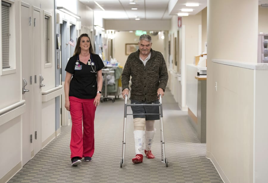 Christina Gay, left, takes a walk with patient Gene Wickstrom, helping him get back on his feet after knee-replacement surgery on April 5.