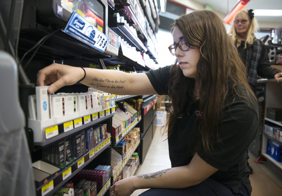 Jacksons Food Stores cashier Ciara Baker stocks a shelf with Juul pods and devices, which resemble USBs. Baker said most customers purchasing Juul pods and devices at the Hazel Dell store are young adults.