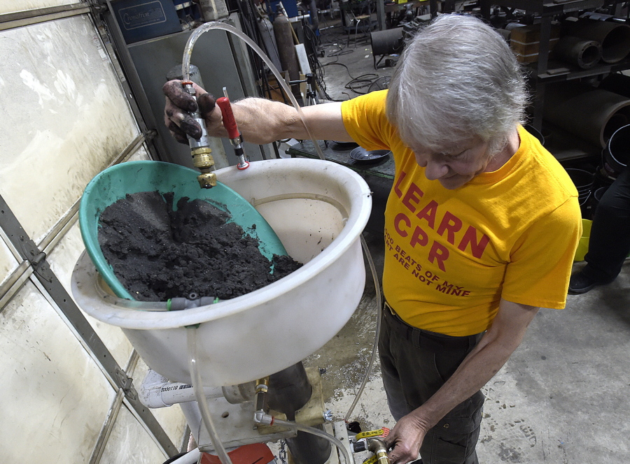 In this Friday April 13, 2018 photo, John Richmond adjusts his water jets while demonstrating his invention called the "Sluice Goose" at his machine shop near Albany, Ore. Richmond poured a pan of black sand mixed with about a half ounce of gold into his machine. Within five minutes the gold was separated from the sand.