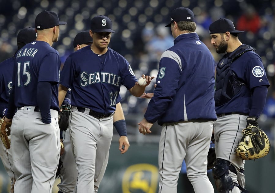 Seattle Mariners starting pitcher Marco Gonzales (32) hands the ball to manager Scott Servais, second from right, during the third inning of a baseball game against the Kansas City Royals at Kauffman Stadium in Kansas City, Mo., Monday, April 9, 2018.