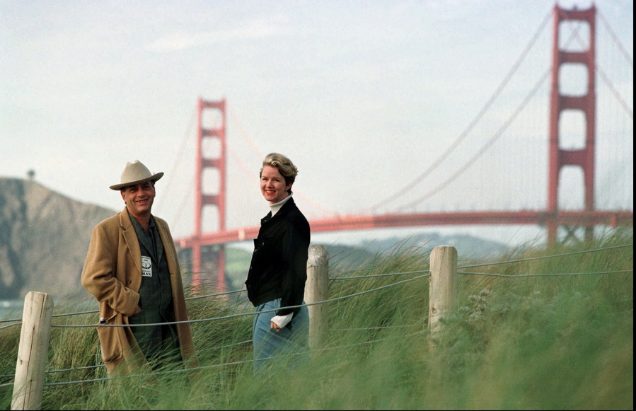FILE - In this March 30, 1998, file photo, Larry Harvey, left, and Marian Goodell, two of the founders of the Burning Man festival walk near Baker Beach in San Francisco with the Golden Gate Bridge in the background. Harvey, the co-founder of the “Burning Man” festival has died. He was 70. Burning Man Project CEO Marian Goodell says Harvey died Saturday, April 28, 2018, morning at a hospital in San Francisco. The cause was not immediately known but he had suffered a stroke on April 4. Harvey created Burning Man on a San Francisco beach in 1986, later moving the annual event to Nevada’s Black Rock Desert.