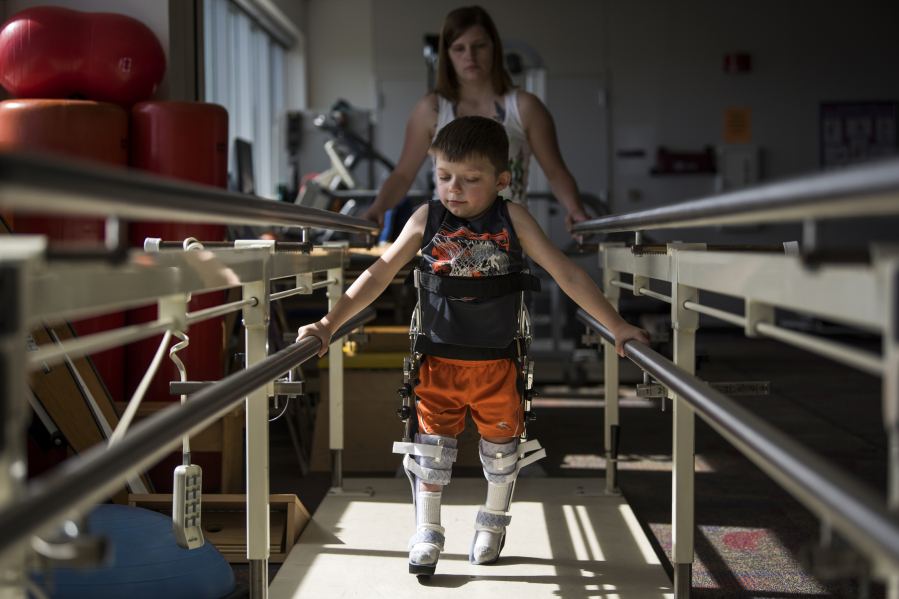 Austin Justin walks in front of his mom, Tabitha Fich, between parallel bars with his new RGO braces at his weekly physical therapy appointment at Shriners Hospitals for Children in Portland in April. “Every week when we go to therapy, his therapist always compliments how well he’s progressing and how fast he’s coming along, because it takes years for kids to be able to even get used to the RGOs,” Fich said. “Austin is just rocking through it.