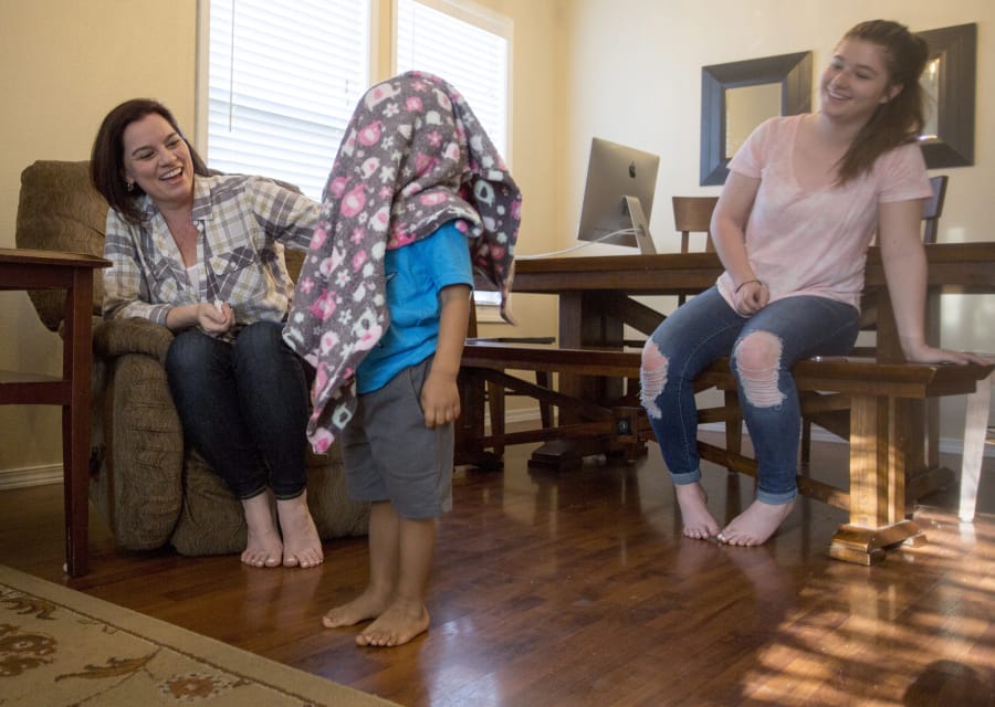 Shannon Williams laughs as her 2½-year-old foster son drapes a blanket over his head. Moriah Williams, 16, right, is one of Shannon Williams’ three biological children.