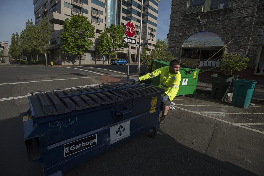 Ryan Mayer of Waste Connections of Washington empties a garbage bin at the corner of West Ninth and Washington streets. A task force of city officials and business owners is proposing new dumpster enclosures and fines to corral garbage.