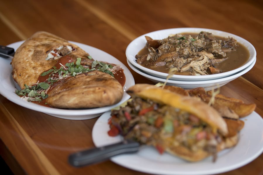 A calzone with meatballs, mozzarella and basil, left, is served with the Brewer’s poutine with shredded pork, top right, and the Peloton steak sandwich at Hopworks Urban Brewery.