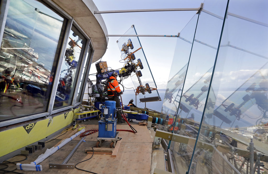 FILE - In this March 20, 2018, file photo, a one-ton glass panel is moved into position on the Space Needle's observation deck in Seattle.  The 56 year-old Space Needle is set to unveil a $100 million renovation next month against the backdrop of a booming tourism industry. Seattle's Wright family, which built and owns the Space Needle, is installing floor-to-ceiling glass in the observation deck and remodeling the restaurant in the first phase of the renovation.