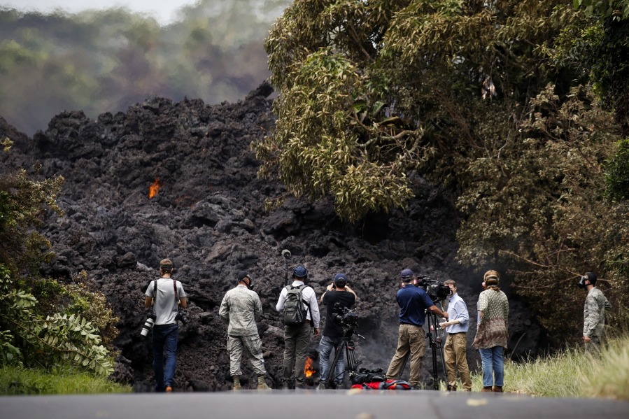Members of the media record a wall of lava entering the ocean near Pahoa, Hawaii, on Sunday. Kilauea volcano, oozing, spewing and exploding on Hawaii’s Big Island, has gotten more hazardous in recent days, with rivers of molten rock pouring into the ocean and flying lava causing the first major injury. (AP Photo/Jae C.
