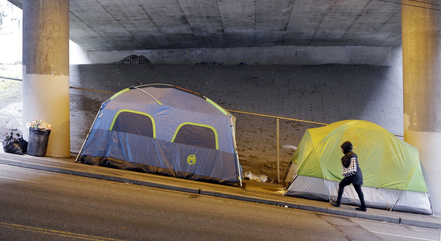 FILE- In this March 8, 2017, file photo, a person walks up a hill next to tents lined up beneath a highway and adjacent to downtown Seattle. Seattle Mayor Jenny Durkan wants to move hundreds more homeless people into tiny homes, emergency shelters and other immediate housing in the next 90 days.