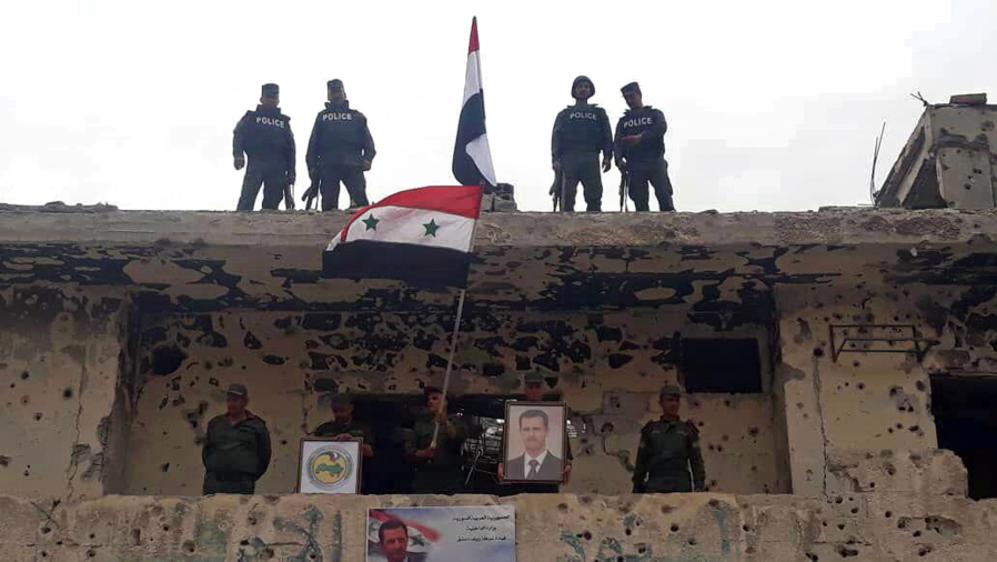 Syrian military and police forces fly their national flags on a damaged building and hold a picture of Syrian President Bashar Assad Tuesday in Damascus, Syria. Syrian state TV said the military is celebrating recapturing the last neighborhoods in Damascus that were held by rebels and the Islamic State group.