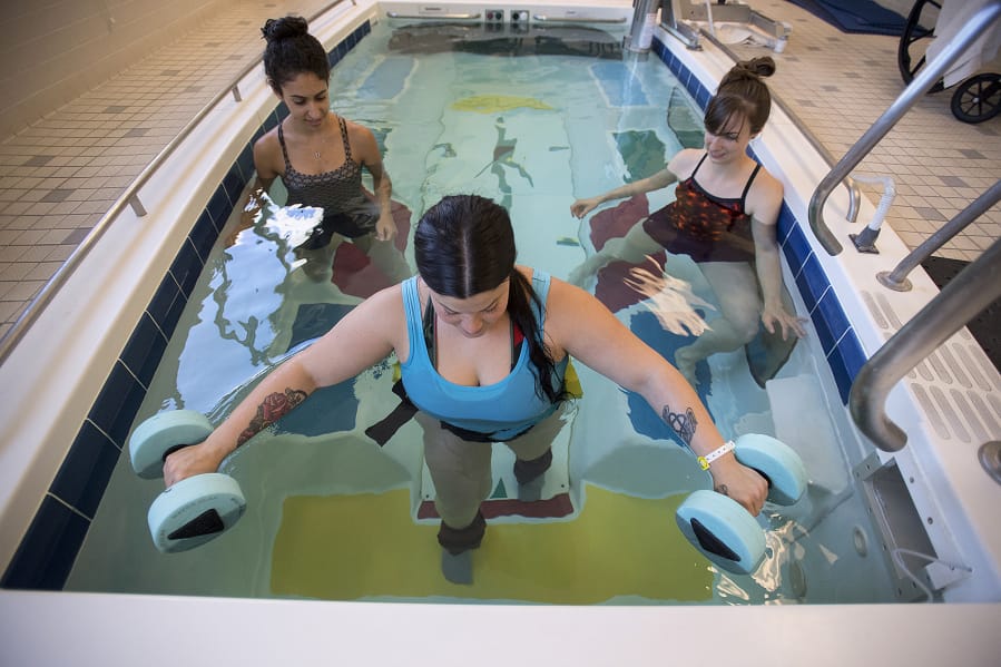 Catherine Martinez of Vancouver, foreground, who mysteriously lost the ability to walk on her birthday in May, practices leg-strengthening exercises with student physical therapist Sabrita Cohen, background left, and physical therapist Jane Gyarmaty at PeaceHealth Southwest Medical Center. Martinez is pictured wearing four-pound weights on each leg as she practices walking up a step in the therapy pool. Martinez has been in the hospital nearly a month, and doctors still don’t know the root cause of Martinez’s ailment.