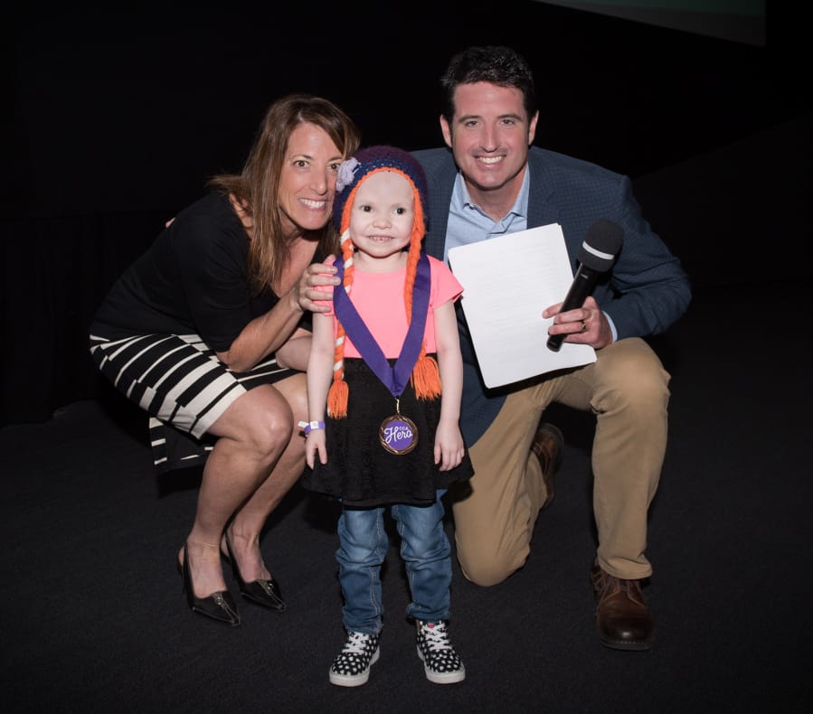 Central Vancouver: Lyla Hopper-Lopez, 4, center, was honored as a Children’s Cancer Association 2018 CCA Hero at an event at the Oregon Museum of Science and Industry hosted by Regina Ellis, association founder and chief joy officer, left, and Drew Carney of KGW-TV.