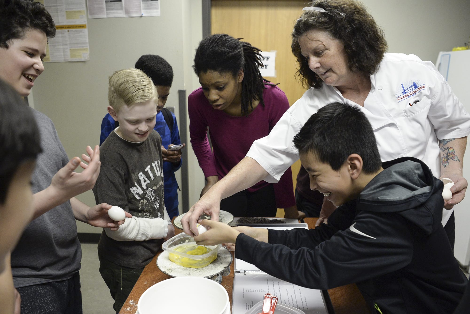 Alison Dolder, department head for professional baking and pastry arts at Clark College, right, helps sixth-grader Eduardo Castellon, right, crack an egg while Eduardo Santos, left, Jaden Cleere and Janoah Stegall watch nearby during a baking lesson at the Boys & Girls Clubs of Southwest Washington in April 2017.