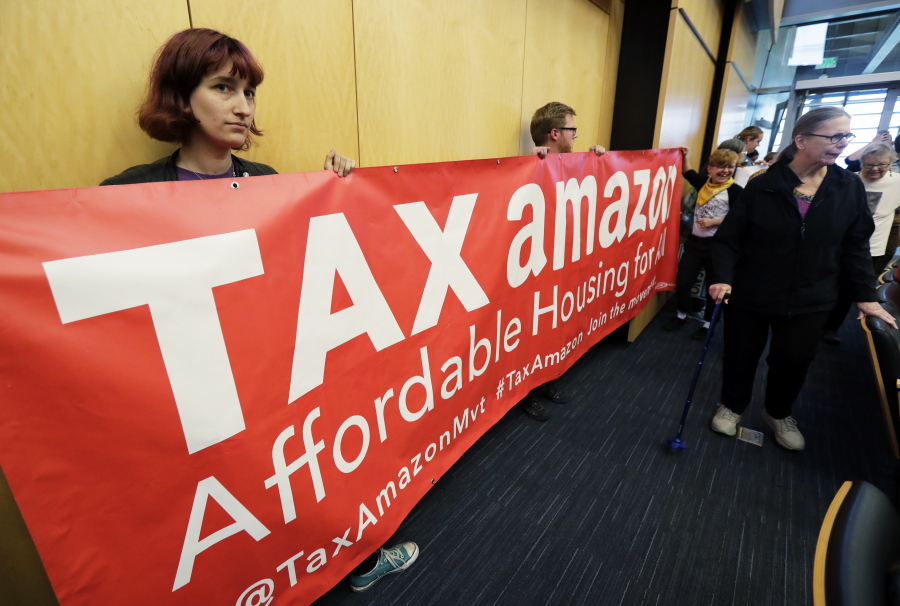 Demonstrators opposing the repeal of a tax on large companies such as Amazon and Starbucks that was intended to combat a growing homelessness crisis hold a sign that reads “Tax Amazon” as they wait for the start of a Seattle City Council meeting, Tuesday, June 12, 2018, at City Hall in Seattle. Members of the Council were expected to vote Tuesday on whether or not to repeal the tax. (AP Photo/Ted S.