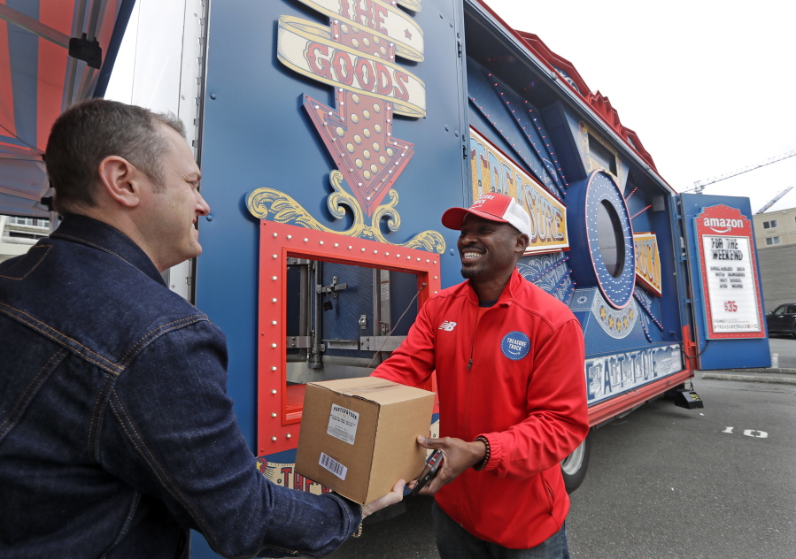 In this May 24, 2018, photo Amazon worker Khayyam Kain, right, hands off a package to a customer at an Amazon Treasure Truck in Seattle. The Treasure Truck is a quirky way for the online retailer to connect with shoppers in person, expand its physical presence and promote itself. Amazon has also used the trucks to try to bring people into Whole Foods, the grocery chain it bought last year. The trucks debuted two years ago and now roam nearly dozens of cities in the United States and England.