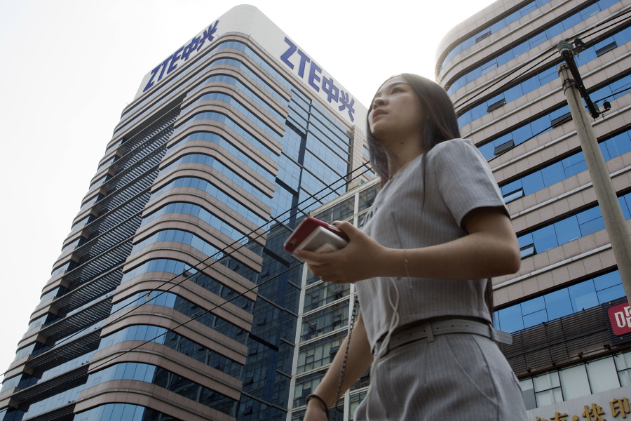 FILE - In this May 8, 2018, file photo, a woman passes by a ZTE building in Beijing, China. Chinese tech giant ZTE Corp.’s chairman promised no further compliance violations and apologized to customers in a letter Friday, June 8, 2018, for disruptions caused by its violation of U.S. export controls, a newspaper reported.